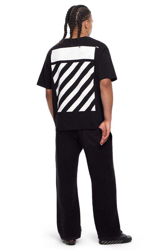 A model shown from the back wearing a black Off-White t-shirt with the signature diagonal striped block on the back, paired with black sweatpants and black sneakers, against a plain white background.#color_black