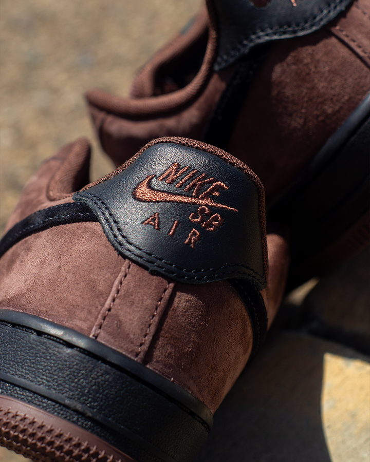 Close-up of a brown suede Nike SB Air sneaker with black leather heel tab and embossed copper-toned Nike logo and text.
