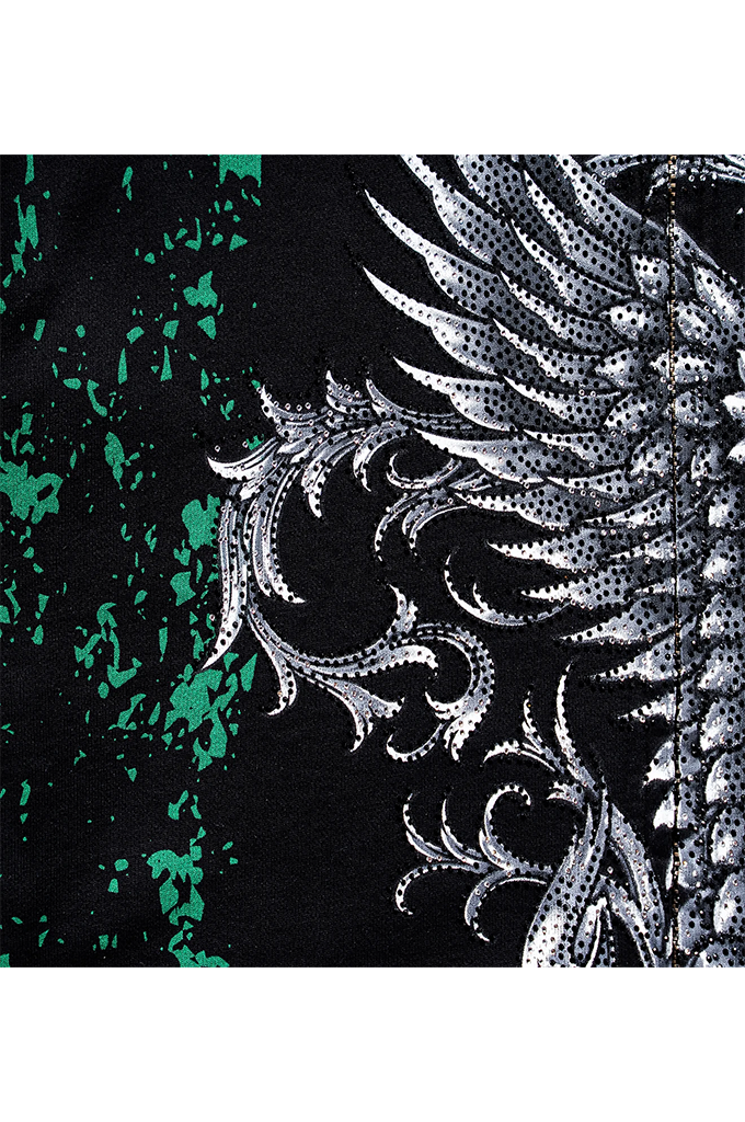A close-up of a black fabric featuring a large white and silver patterned wing design alongside a textured green and black splatter pattern.