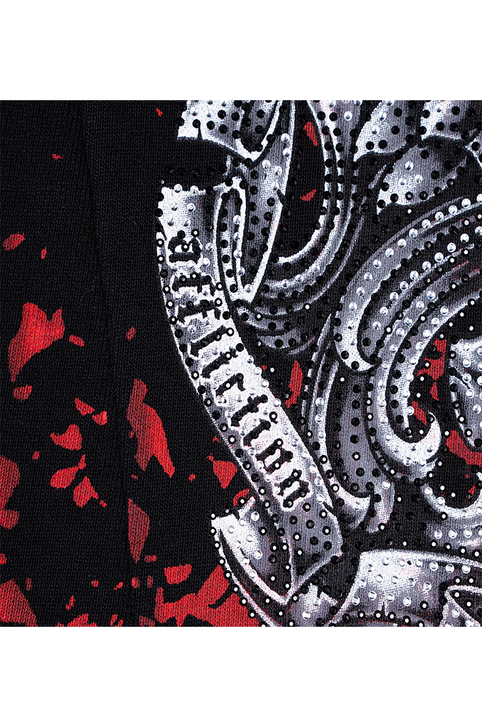 Close-up of a black fabric with a large metallic silver ornamental pattern and scattered red splatter accents.