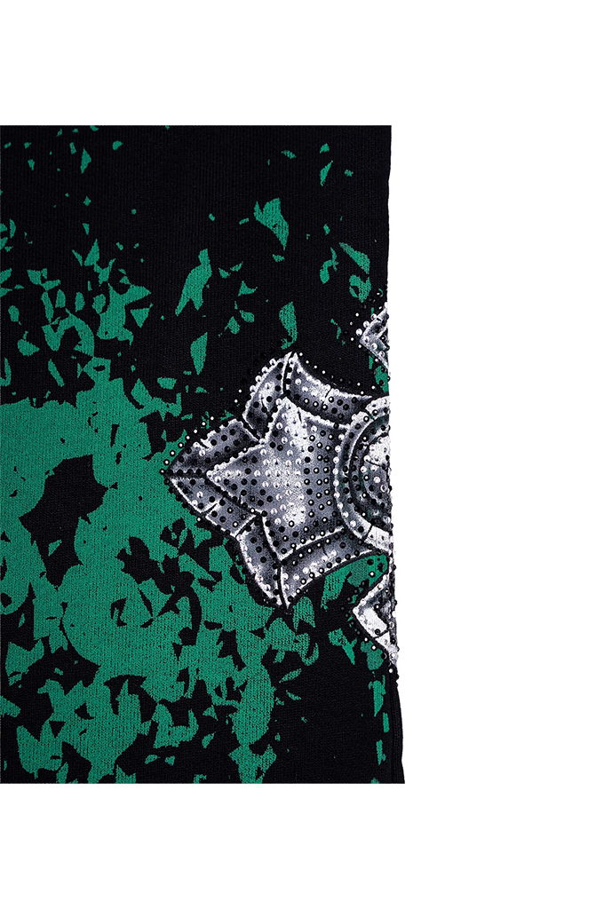 A close-up of a black and green abstract patterned fabric with a metallic silver textured emblem on the right side, set against a plain white background.