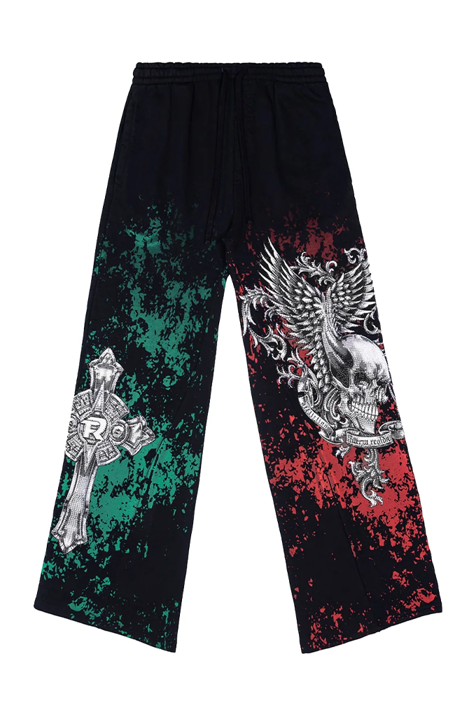Black wide-leg sweatpants featuring a distressed green splatter on the left leg and a distressed red splatter on the right leg, decorated with a silver-toned cross graphic on the left and a detailed silver skull and eagle graphic on the right.