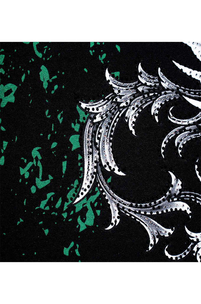 A close-up of a black fabric featuring a white baroque scroll pattern and green paint-splatter accents.