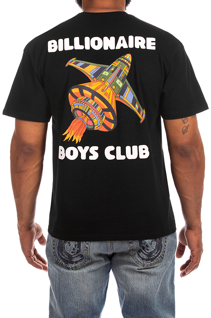 A man wearing a black t-shirt from the back, featuring a colorful retro spaceship graphic and the text 'BILLIONAIRE BOYS CLUB' in white. He is also wearing blue jeans with a graphic on the back pocket.