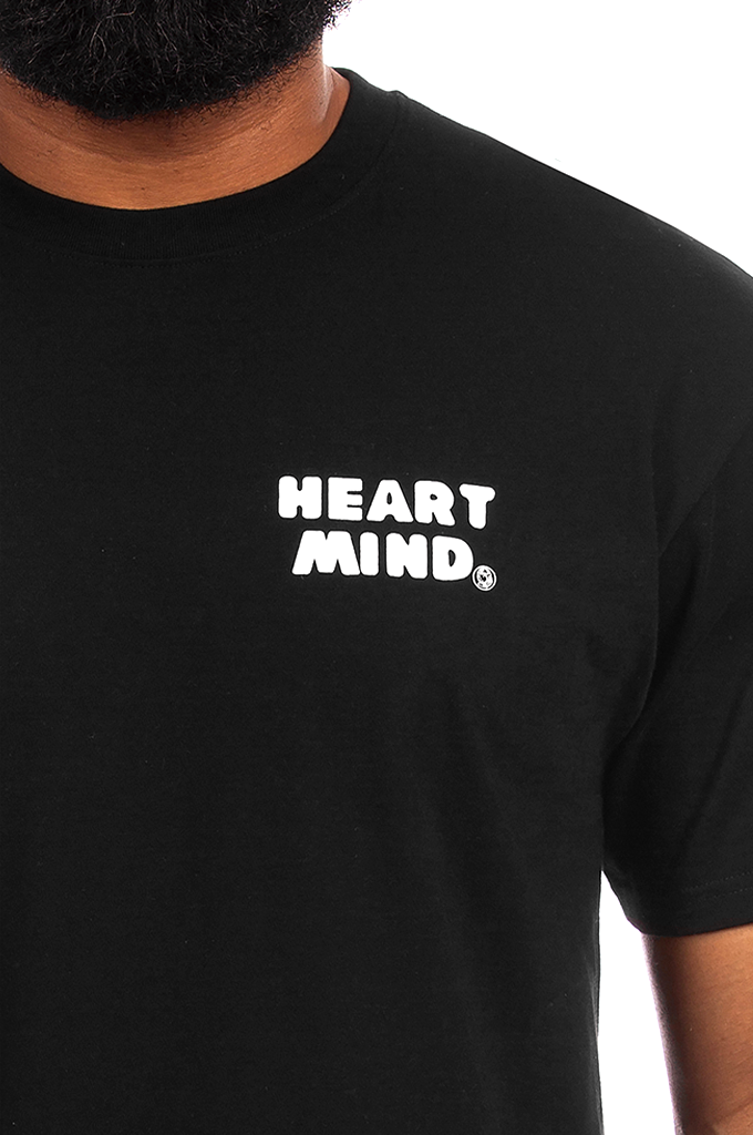 A close-up of a person wearing a black short-sleeve t-shirt with the words 'HEART MIND.' printed in white block letters on the chest.