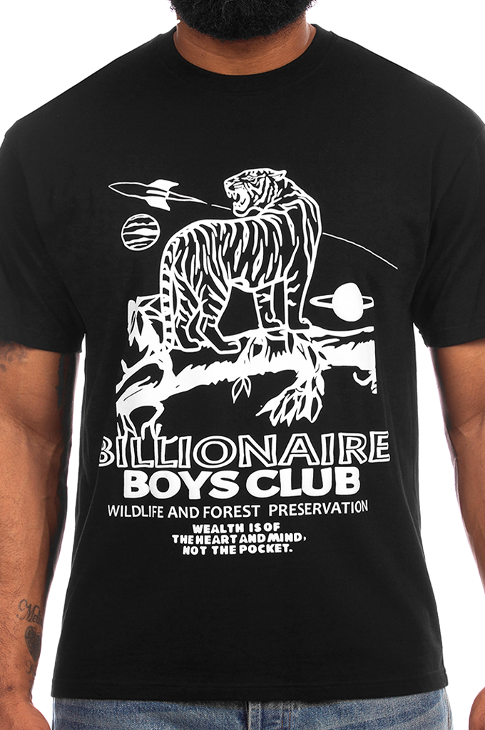 A man wearing a black short-sleeve graphic t-shirt with a white print of a tiger, planets, and the text 'BILLIONAIRE BOYS CLUB WILDLIFE AND FOREST PRESERVATION'.