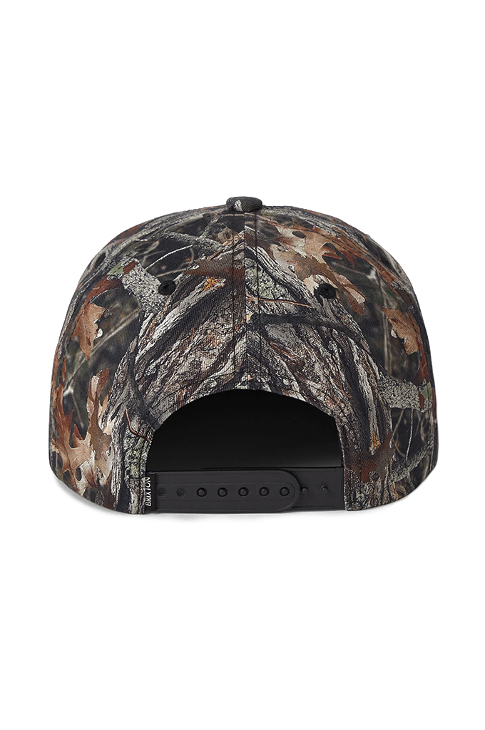 Rear view of a Brixton Division Netplus snapback hat featuring a realistic tree and leaf camouflage pattern with a black adjustable plastic snap closure.
