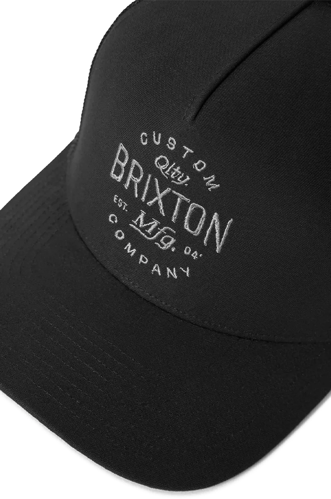 A black 5-panel Brixton Fremont C NP MP trucker hat featuring a curved brim, mesh back panels, and a white circular "Brixton Qlty. Mfg. Company" graphic logo on the structured front.
