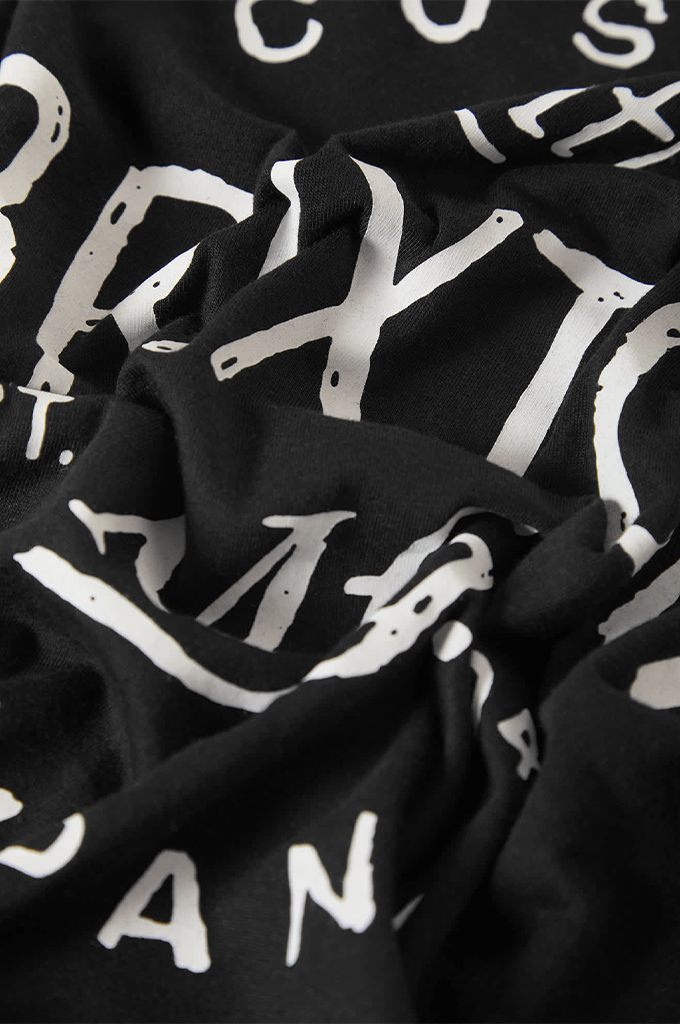 A close-up view of a folded or wrinkled piece of black fabric. The material features large, bold white letters printed across it in a slightly distressed, hand-drawn or stencil-like font. Portions of words like "BRIXTON" and "PAN" are visible among the folds.