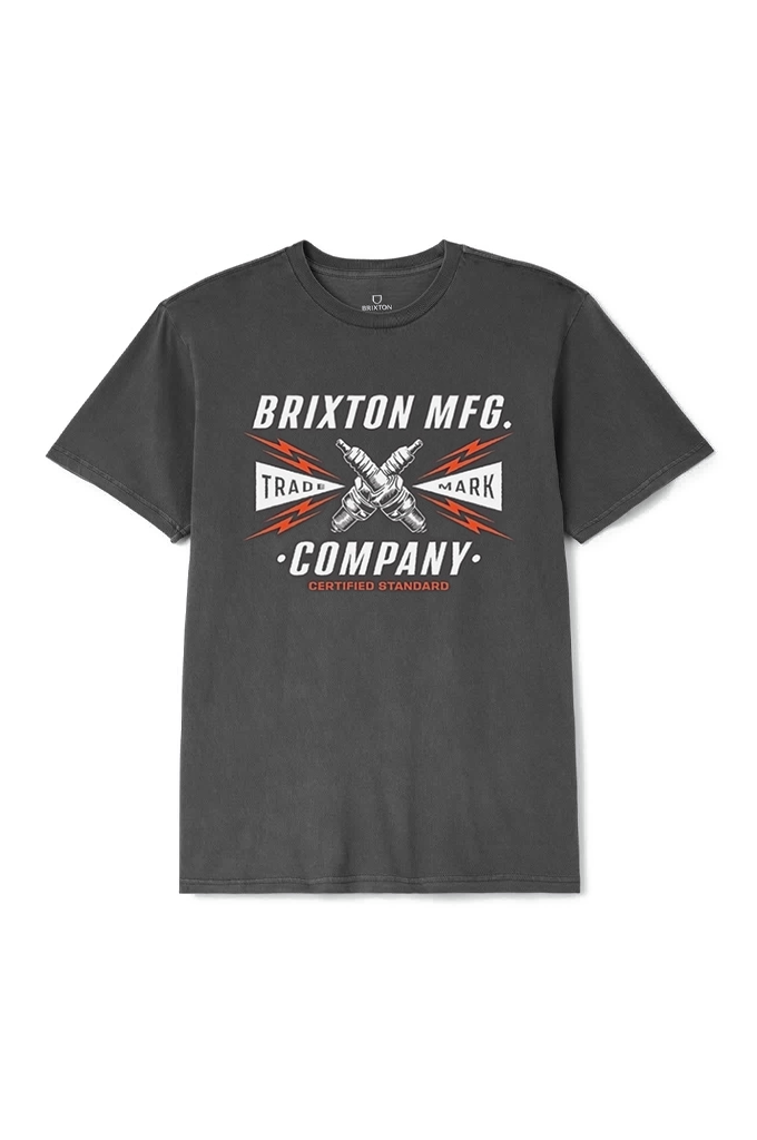 A dark grey short-sleeved t-shirt is centered against a plain white background. The shirt features a graphic design on the chest with the text "BRIXTON MFG." arched over two crossed silver spark plugs. Red lightning bolts radiate from behind the spark plugs. Flanking the graphic are two white triangular banners: the left one reads "TRADE" and the right one reads "MARK". Below the spark plugs, the word "COMPANY" is printed in large white letters, with a small subtitle underneath reading "CLOTHING STANDARD" i
