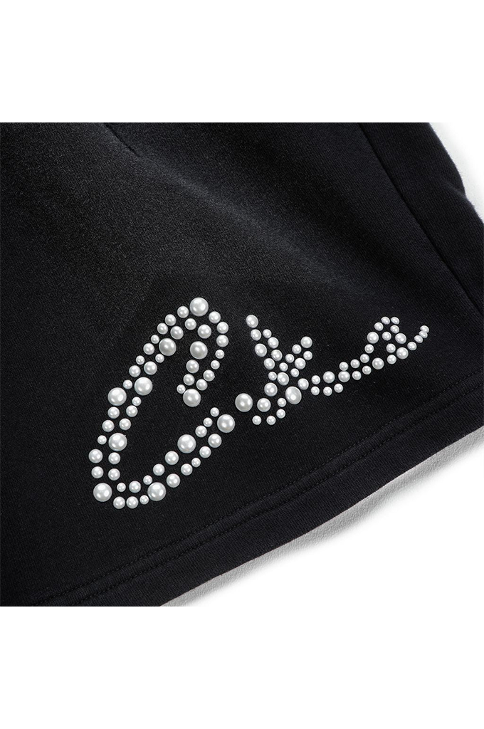 Close-up of a black garment featuring a large cursive script logo outlined with white rhinestones on the lower left side.