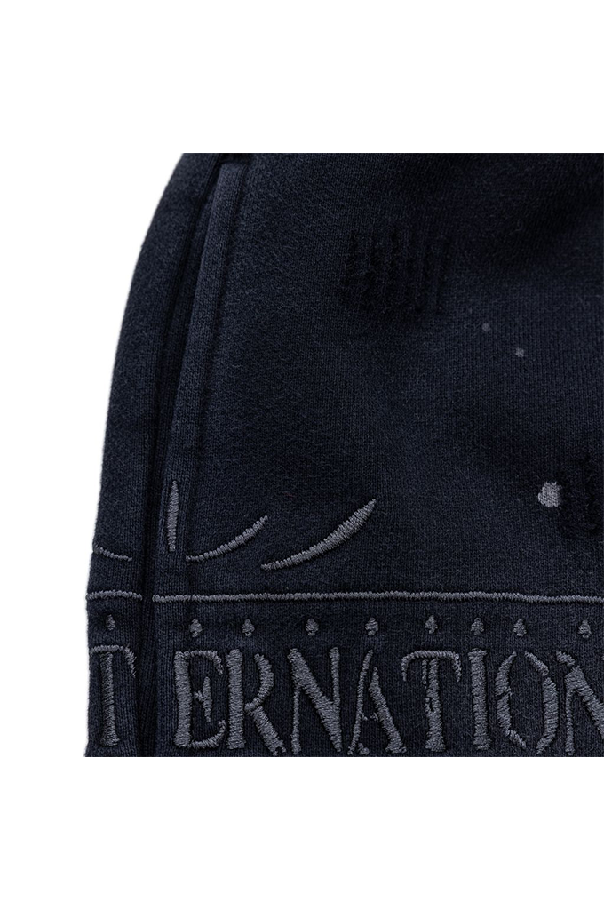 Close-up of a dark navy fabric product with tonal embroidered lettering and decorative stitching, shown against a white background.