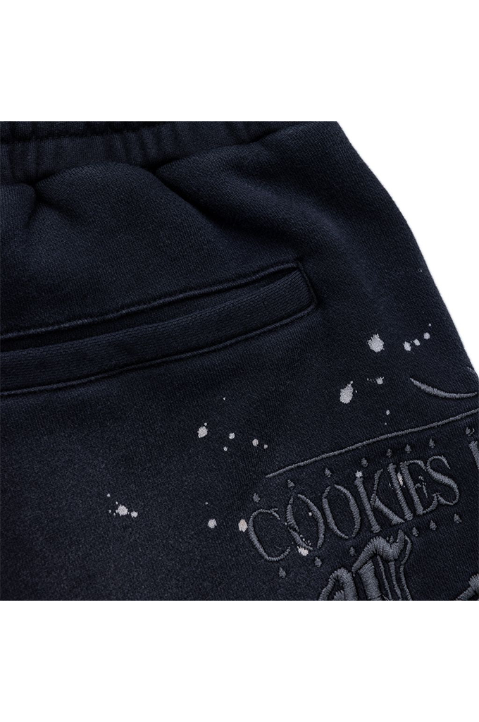 Close-up of dark navy sweatpants with a side pocket and a distressed graphic that reads 'COOKIES' with paint splatter details.