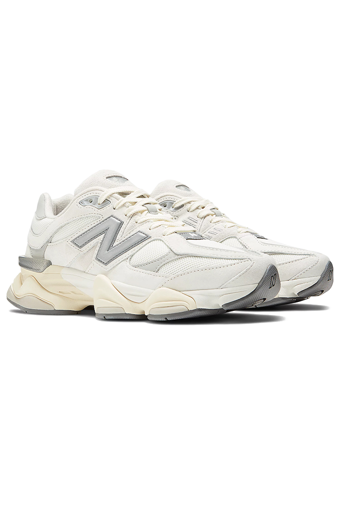 A pair of white and cream New Balance 9060 lifestyle sneakers with grey and silver accents. The shoes are angled diagonally to the right on a plain white background, highlighting their chunky, sculpted wavy midsole, light mesh upper with suede overlays, and the prominent silver signature "N" logo on the outer side. #color_white-grey-sea-salt-concrete