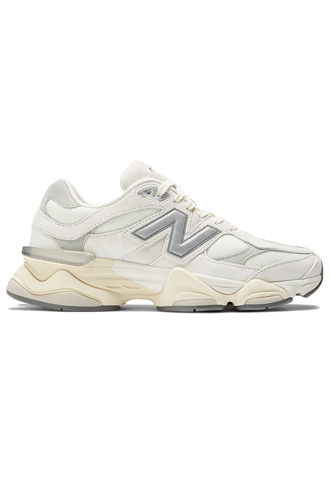 A side-profile view of a New Balance 9060 sneaker. The shoe features a retro-futuristic style with a chunky, sculpted cream and grey midsole. The upper is made of off-white mesh and suede overlays, with a metallic silver "N" logo on the side. #color_white-grey-sea-salt-concrete