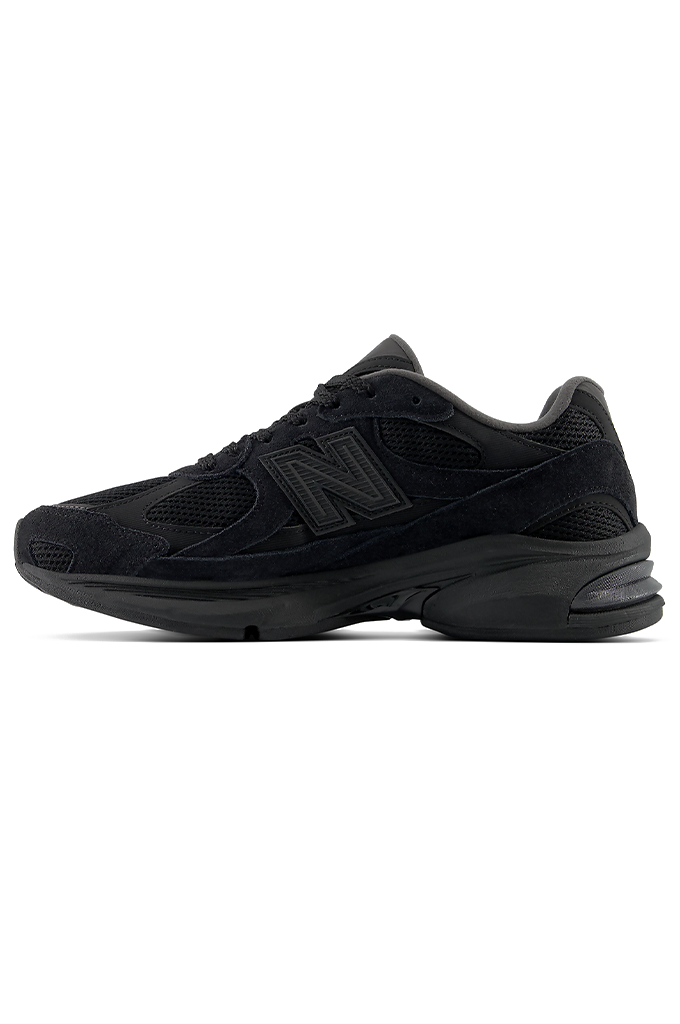 A profile view of a New Balance 2010 sneaker in an all-black colorway. The running-style shoe features a dark mesh base with suede overlays, matching black laces, and the signature New Balance "N" logo on the side panel. The entire sneaker, including the thick, segmented midsole and rubber outsole, is uniformly black.#color_black-black