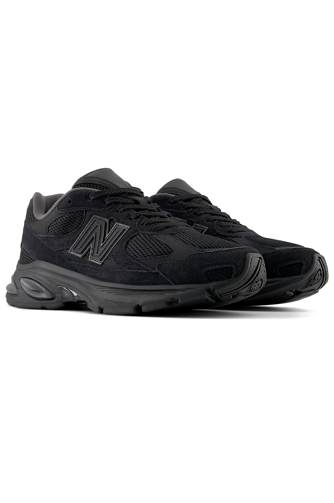 An angled view of a New Balance 2010 sneakers in an all-black colorway. The running-style shoe features a dark mesh base with suede overlays, matching black laces, and the signature New Balance "N" logo on the side panel. The entire sneaker, including the thick, segmented midsole and rubber outsole, is uniformly black.#color_black-black