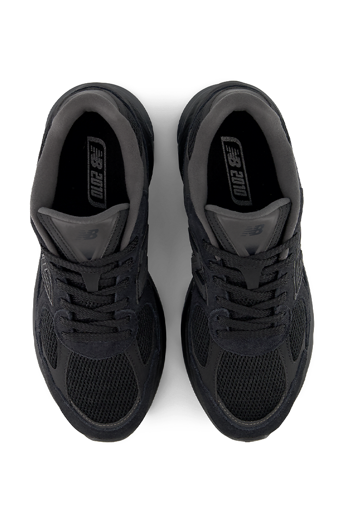 A top view of a New Balance 2010 sneaker in an all-black colorway. The running-style shoe features a dark mesh base with suede overlays, matching black laces, and the signature New Balance "N" logo on the side panel. The entire sneaker, including the thick, segmented midsole and rubber outsole, is uniformly black.#color_black-black