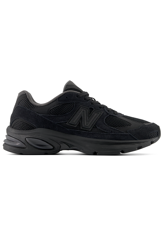 A profile view of a New Balance 2010 sneaker in an all-black colorway. The running-style shoe features a dark mesh base with suede overlays, matching black laces, and the signature New Balance "N" logo on the side panel. The entire sneaker, including the thick, segmented midsole and rubber outsole, is uniformly black.#color_black-black