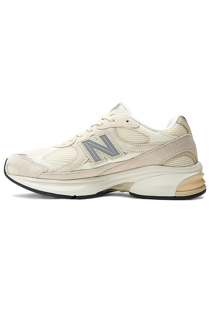 A New Balance sneaker featuring a modern chunky design in shades of grey, cream, and off-white. The shoe has a textured mesh upper with overlapping suede panels, a prominent grey "N" logo on the side, and a thick, multi-layered midsole with a hint of peach coloration near the heel.#color_timberwolf-turtledove