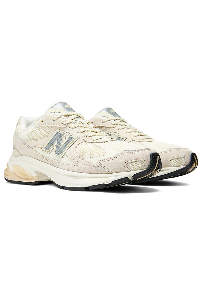 New Balance sneakers featuring a modern chunky design in shades of grey, cream, and off-white. The shoe has a textured mesh upper with overlapping suede panels, a prominent grey "N" logo on the side, and a thick, multi-layered midsole with a hint of peach coloration near the heel.#color_timberwolf-turtledove