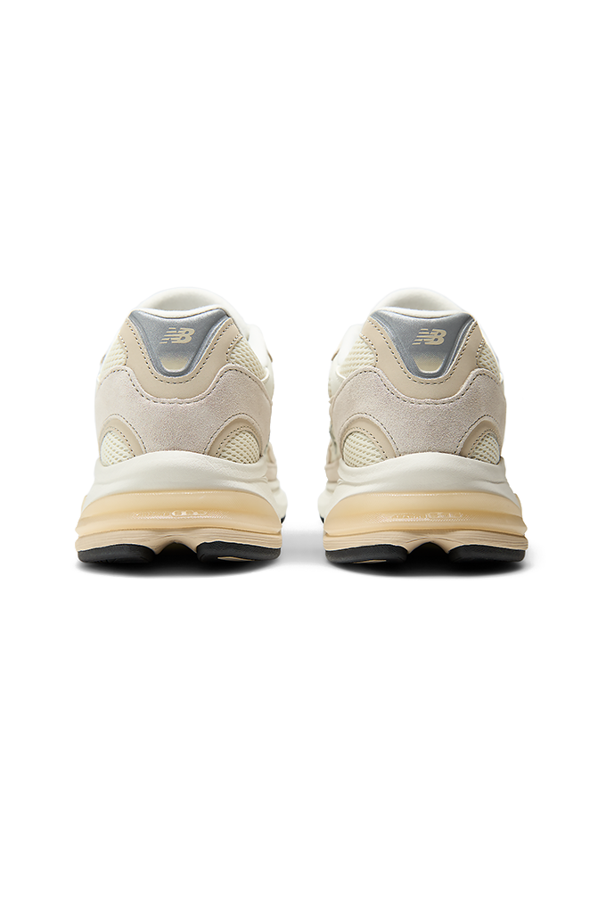 A back view of New Balance sneakers featuring a modern chunky design in shades of grey, cream, and off-white. The shoe has a textured mesh upper with overlapping suede panels, a prominent grey "N" logo on the side, and a thick, multi-layered midsole with a hint of peach coloration near the heel.#color_timberwolf-turtledove