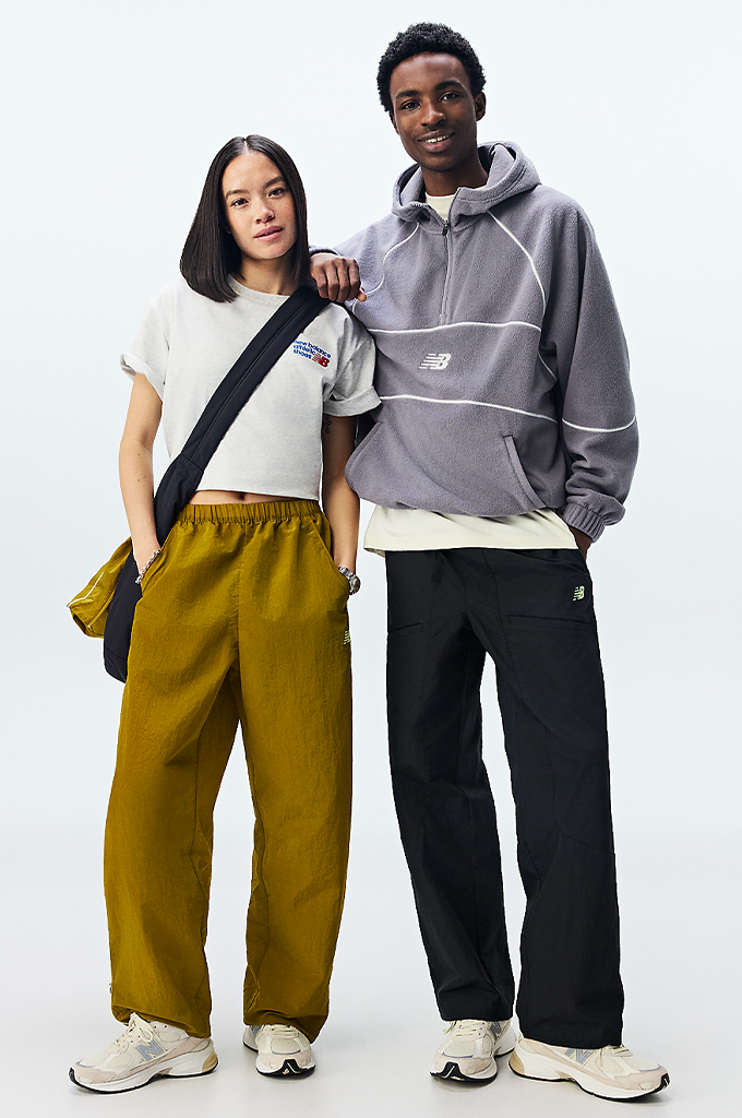 A guy and girl standing wearing New Balance sneakers featuring a modern chunky design in shades of grey, cream, and off-white. The shoe has a textured mesh upper with overlapping suede panels, a prominent grey "N" logo on the side, and a thick, multi-layered midsole with a hint of peach coloration near the heel.#color_timberwolf-turtledove