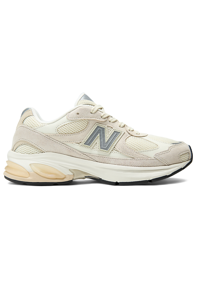 A New Balance sneaker featuring a modern chunky design in shades of grey, cream, and off-white. The shoe has a textured mesh upper with overlapping suede panels, a prominent grey "N" logo on the side, and a thick, multi-layered midsole with a hint of peach coloration near the heel.#color_timberwolf-turtledove