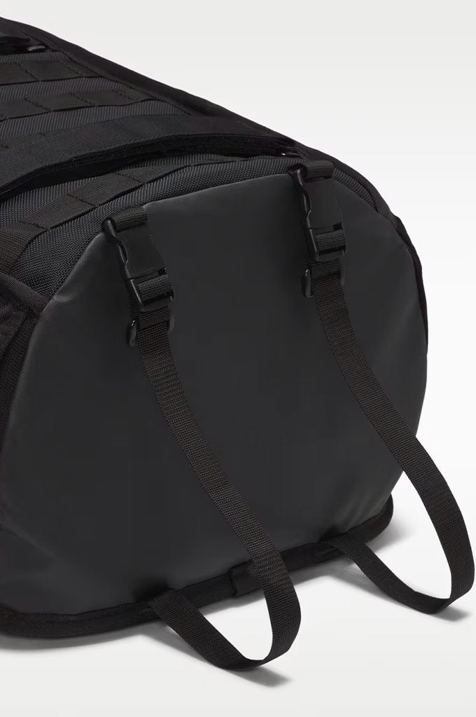 Close-up of a black duffel bag showing the side panel, zipper closure, and adjustable shoulder straps against a light gray studio background.#color_black