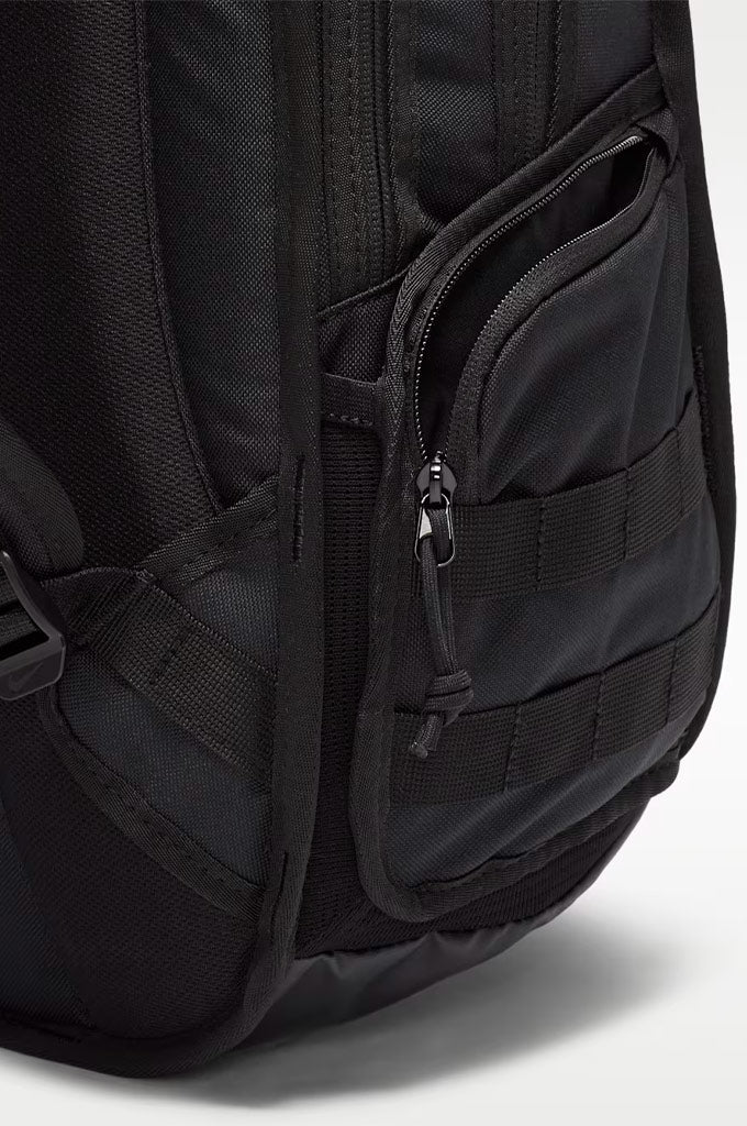Close-up of a black backpack showing the side pocket with a zipper and webbing details against a light gray background.#color_black