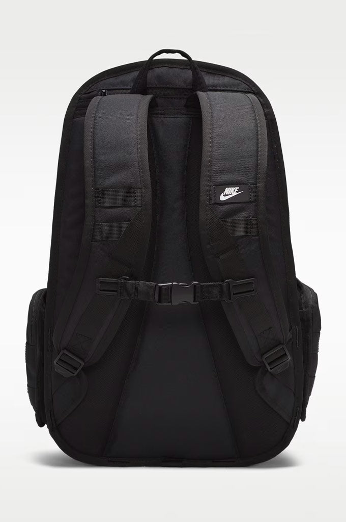 Black Nike backpack shown from the back, featuring padded shoulder straps, a central buckle strap, side pockets, and a small white Nike swoosh logo on the upper right side.#color_black