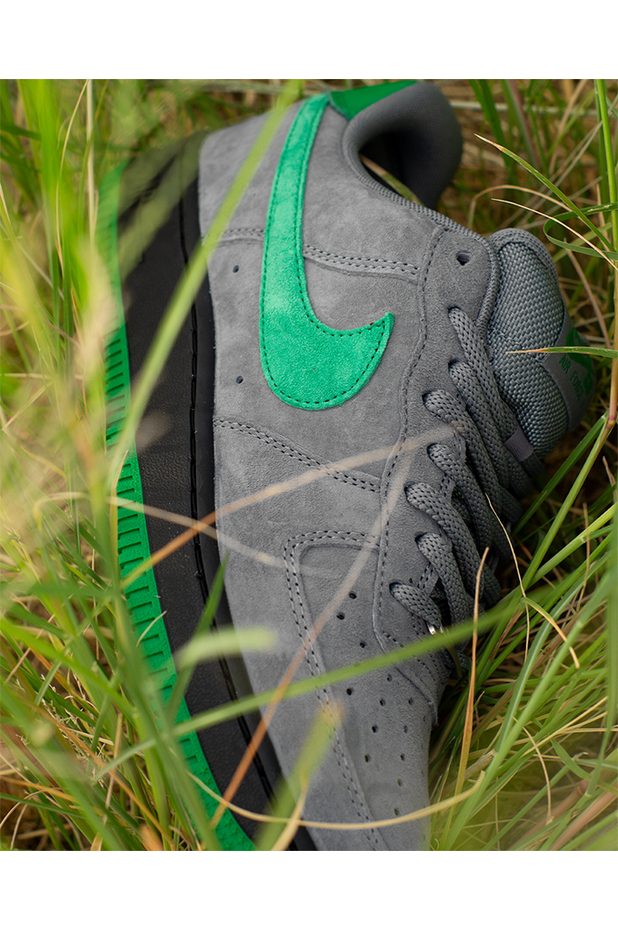Nike SB Air Force 1 Low SE Nocturnal City Pack sneakers in cool grey suede with a court green swoosh and black midsole laying in grass. 