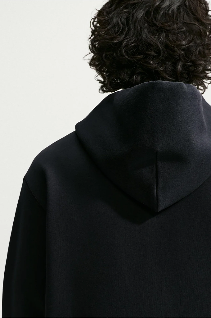 Close-up back view of a person wearing a black hooded sweatshirt against a plain light background.