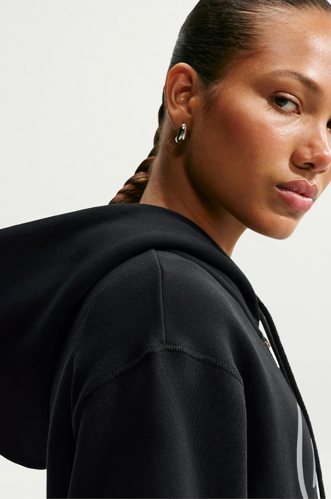 Close-up side profile of a woman wearing a black hooded sweatshirt against a light gray studio background.