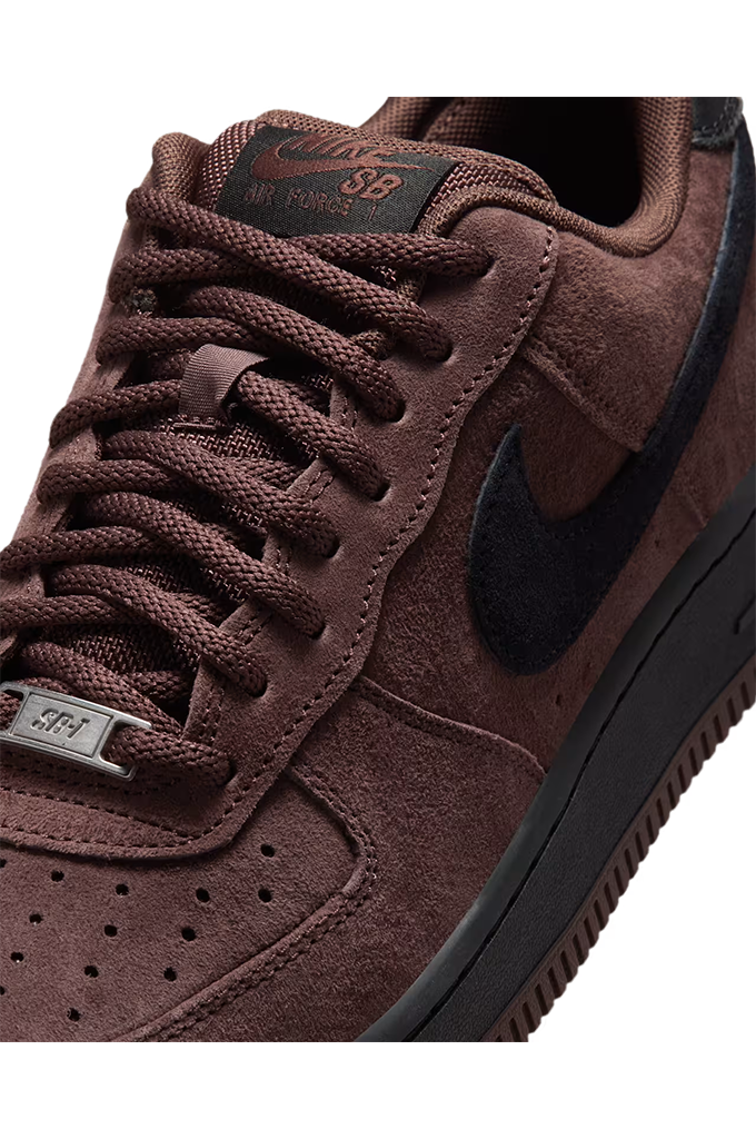 Close-up of a Nike Air Force 1 Low sneaker in dark brown suede with a black Swoosh and black midsole, featuring a metallic silver SFA (San Francisco 49ers) patch on the tongue.