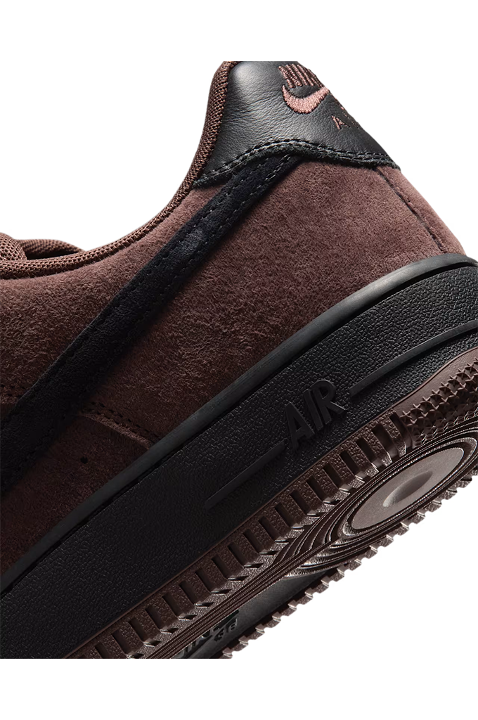Close-up of a Nike sneaker in dark brown suede and black leather, showing the side profile with a black midsole and textured sole.