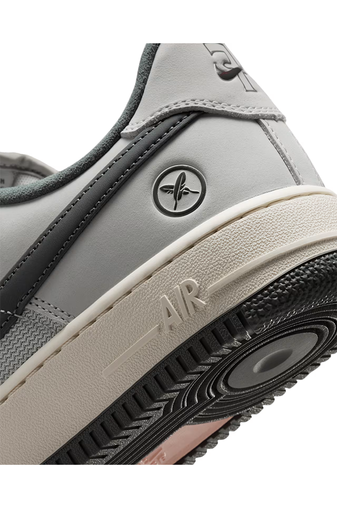 Close-up of a Nike Air Force 1 Low sneaker in gray leather with a black outsole and a beige midsole, showing the side logo and 'AIR' embossed on the midsole.