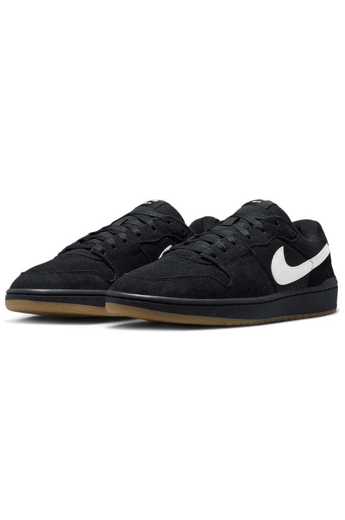 A pair of Nike low-top sneakers in black suede and leather, featuring a prominent white Swoosh on the side and a gum brown sole, set against a plain white background.