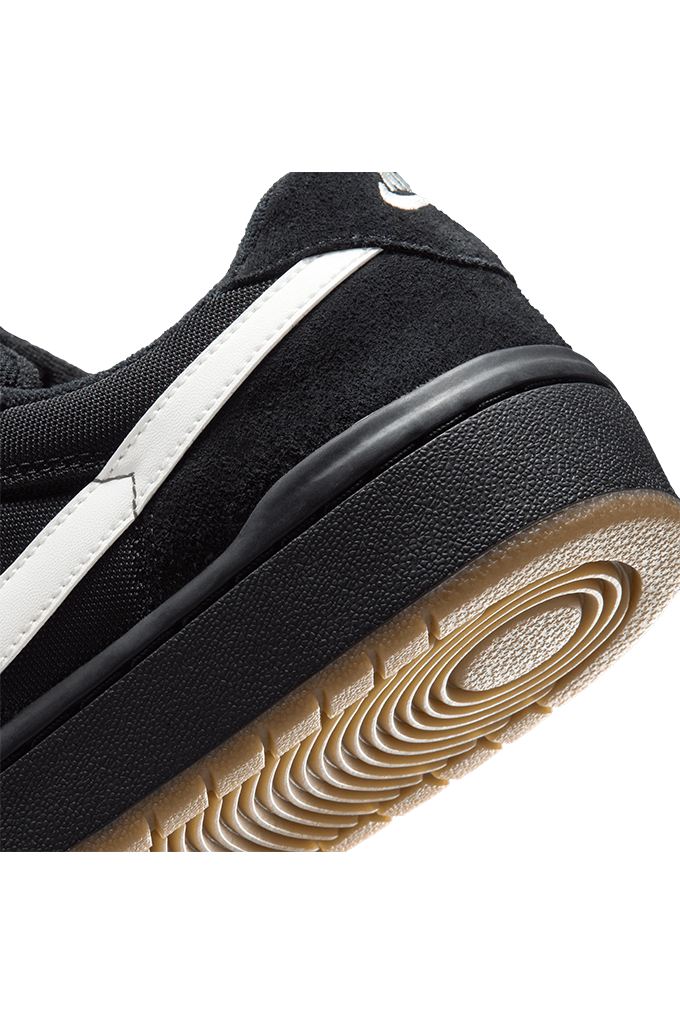 Close-up of a black Nike sneaker showing the side profile, white Nike Swoosh, black rubber midsole, and a brown gum outsole on a white background.