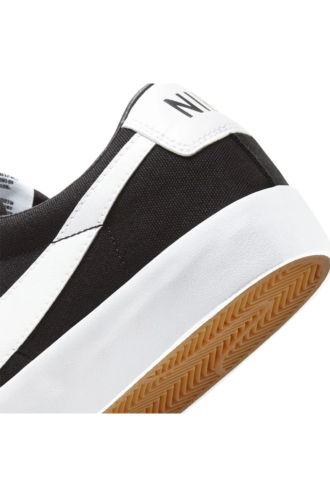 Close-up of a Nike sneaker showing the black canvas upper, white leather side stripe, white heel tab with black Nike lettering, and a brown gum outsole on a white background.#color_black-white-black