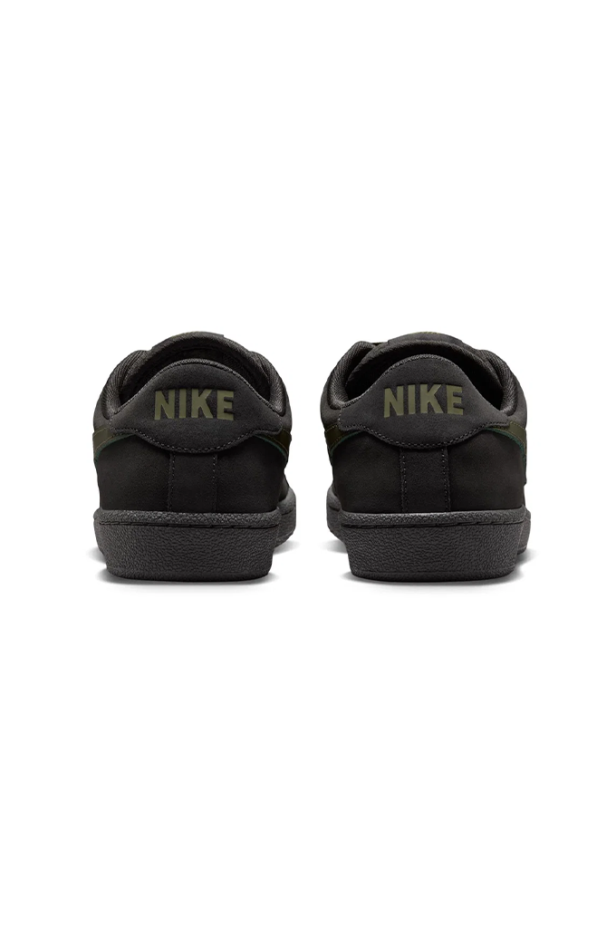 A pair of black Nike low-top sneakers shown from the back, featuring olive green 'NIKE' lettering on the heel tab and a matching black sole, set against a plain white background.