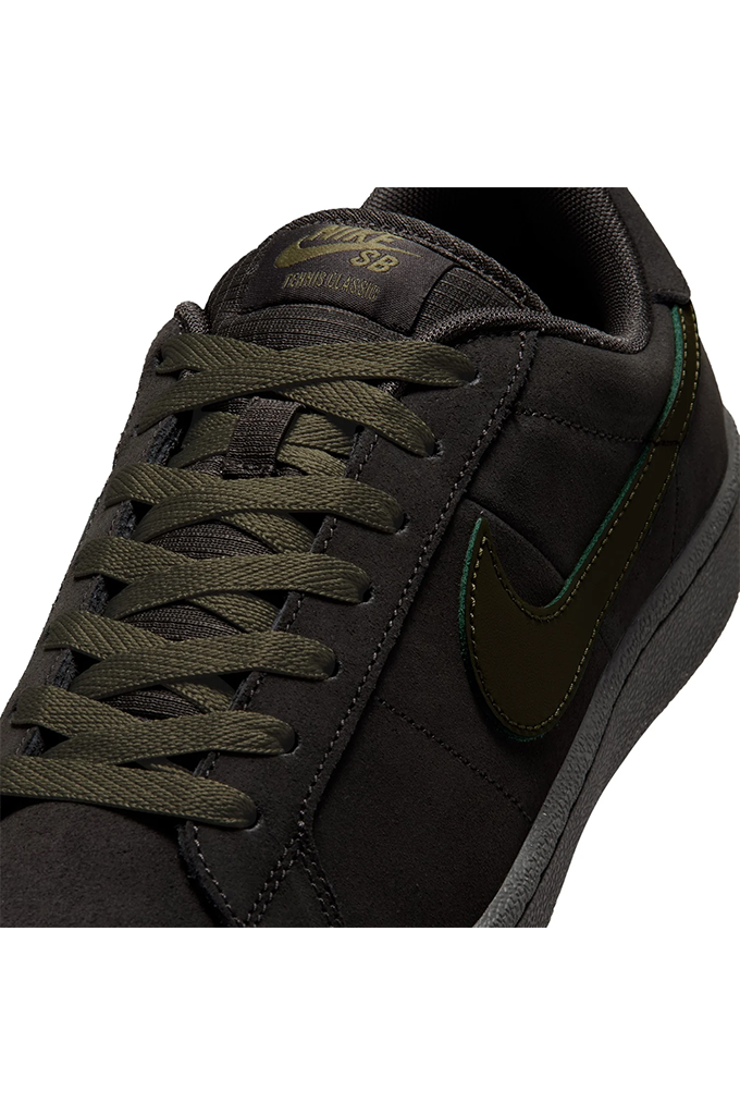 A close-up of a Nike SB  sneaker in black suede and mesh with olive green laces, a dark olive green Swoosh, and subtle green piping details.