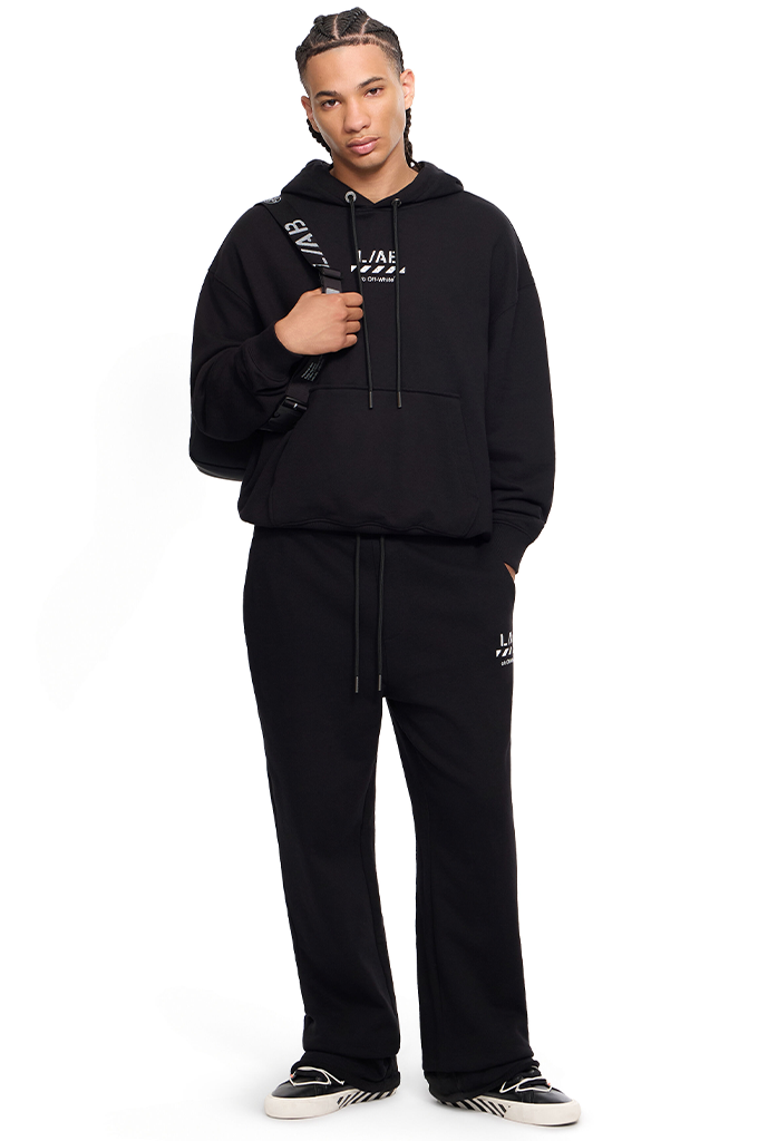 A model wearing a black Givenchy hoodie and matching sweatpants with white logo details, standing against a plain white background.