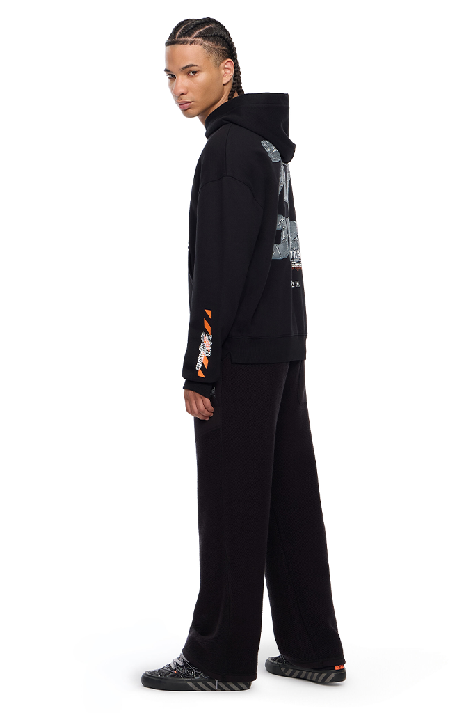 A model wearing a black hooded sweatshirt and matching wide-leg sweatpants, shown from a side profile against a solid white background.#color_black