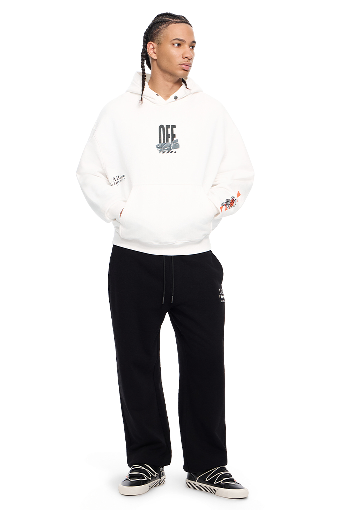 A model wearing a white Off-White pullover hoodie with a black graphic print on the chest, paired with black sweatpants and black-and-white sneakers, set against a plain white background.#color_white