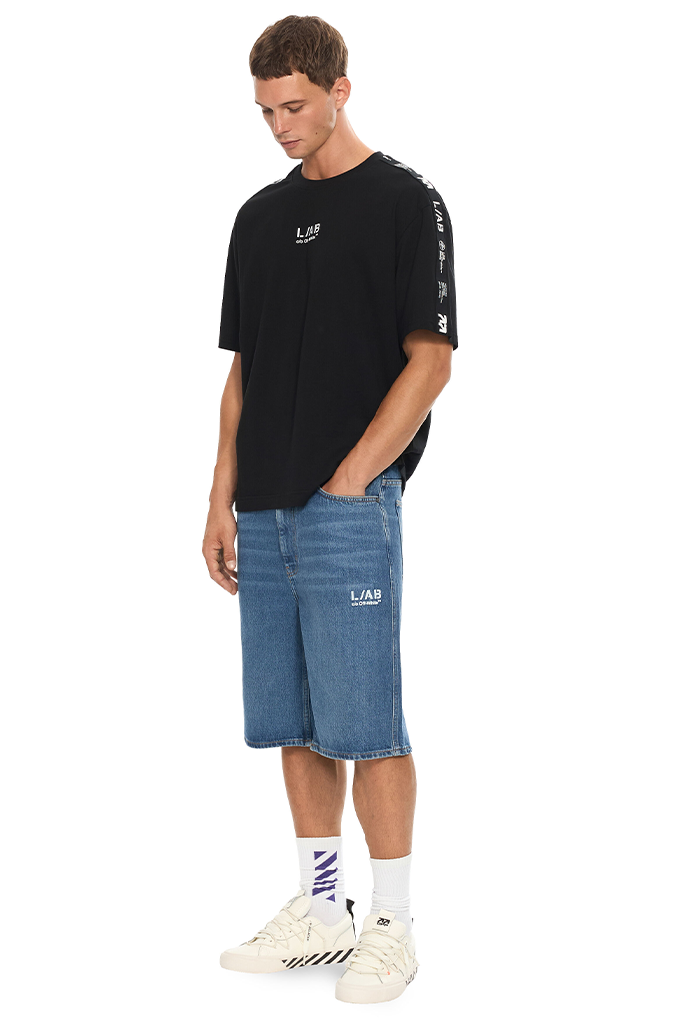 Man wearing blue denim shorts and black shirt on a white background. 