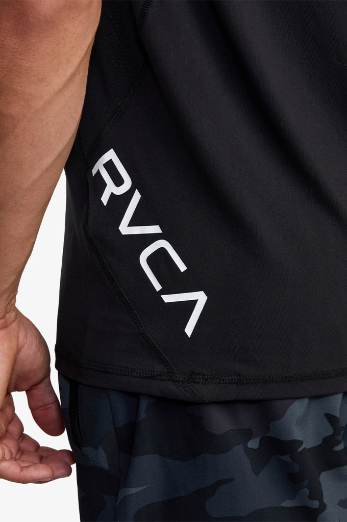 Close-up of a black athletic top worn by a model, featuring a large white RVCA logo printed vertically on the side, paired with dark camouflage shorts.