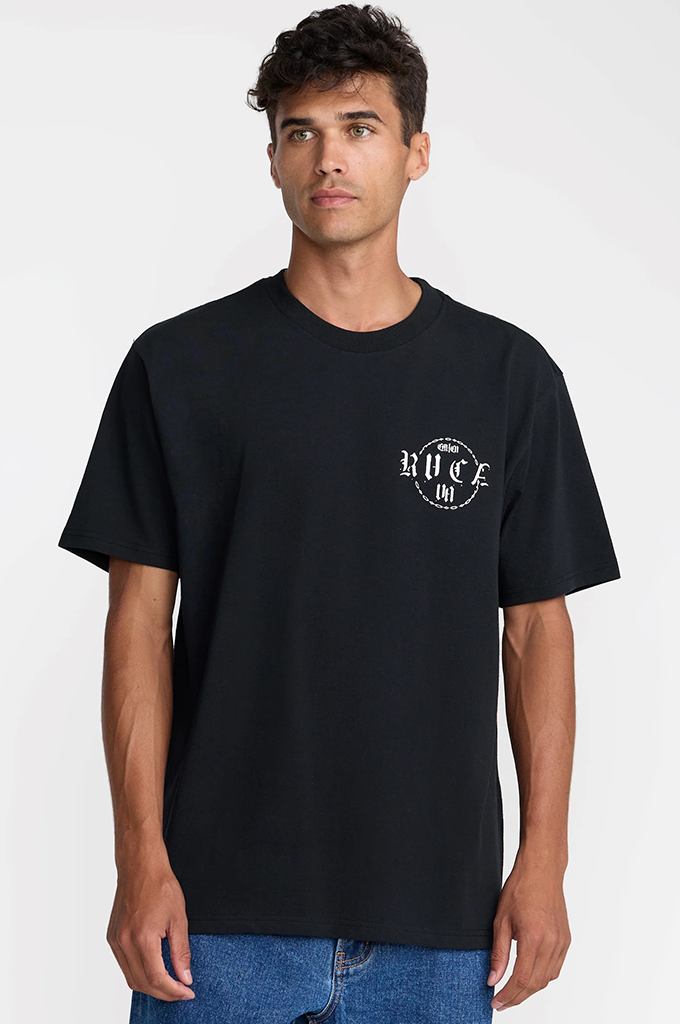 A man wearing a black short-sleeve t-shirt with a white circular 'RVCA' graphic on the left chest, paired with blue jeans, against a light gray studio background.