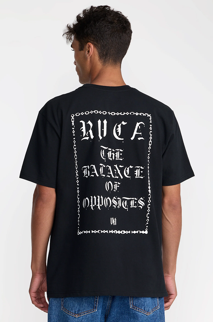 A man wearing a black short-sleeve t-shirt from the back, featuring a large white graphic print with gothic lettering and a chain border. The text reads 'RVCA'.