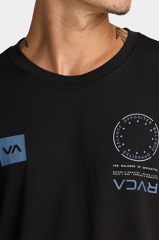 Close-up of a man wearing a black RVCA t-shirt, showing the chest graphics including a blue square logo on the left chest and a circular white graphic with blue text on the right chest.
